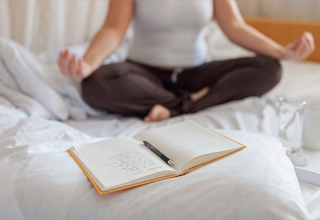 A woman in bed meditates while holding a book with future plans in front of her