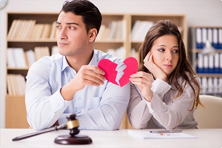 A woman and a man hold a broken heart symbolizing the separation between them