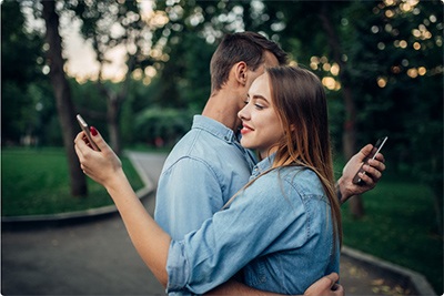 A man and a woman in the park are hugging and holding their phones